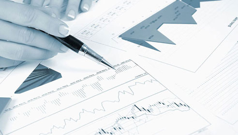 Close up, greyscale photograph of printed charts and a female hand holding a pen