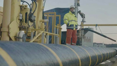 Photograph of a worker on a ship. There is a large cable in the foreground