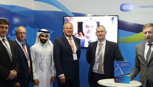 Photograph of six men standing in front of a screen with another an on it.