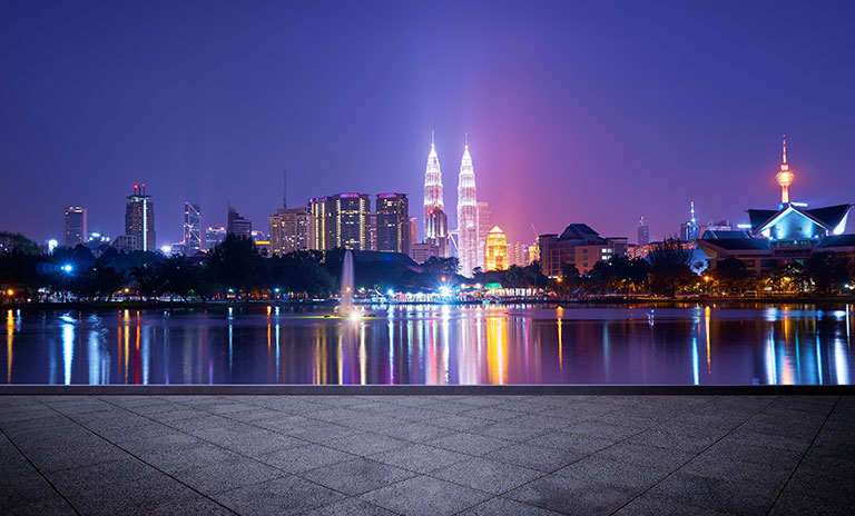 Photograph of a city skyline at night with two towers illuminated and a river in the foreground