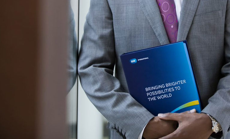 Close photograph of male hands holding a hard cover folder with the words 'Bringing Brighter Possibilities to the World' printed on the front along with the ESB International logo