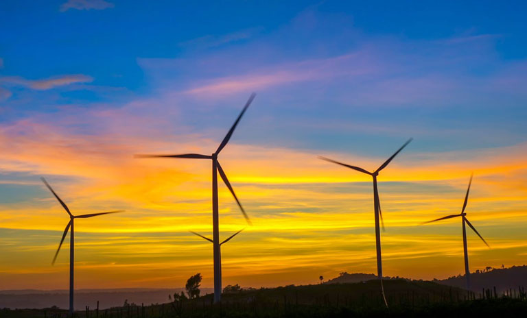 Photograph of wind turbines silhouetted against a sunset background