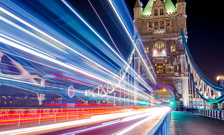 Photograph of London bridge tower at nighttime with motion blur of vehicle lights in the foreground