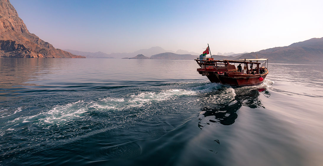 Photograph of a wooden boat on a still body of water with mountains in the distance