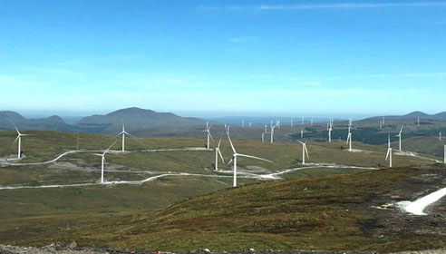 Photograph of a windfarm on top of mountains with blue sky in the background