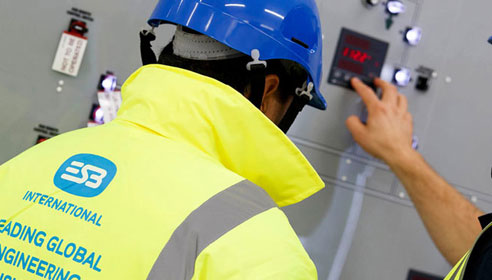 Photograph of two men in hard hats and high vis jackets. Their backs are to the camera and the man on the right is toughing a button on the wall panels