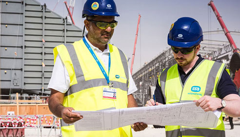 Image of two men in high vis vests and hard hats looking at some drawings on a building site