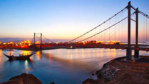 Photograph of a bridge over a river and leading into a city taken at night