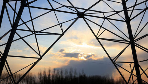 Photograph of a section of an electricity pylon silhouetted against a sunset