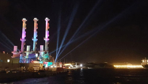 Image of a power station lit up with coloured lights at night time