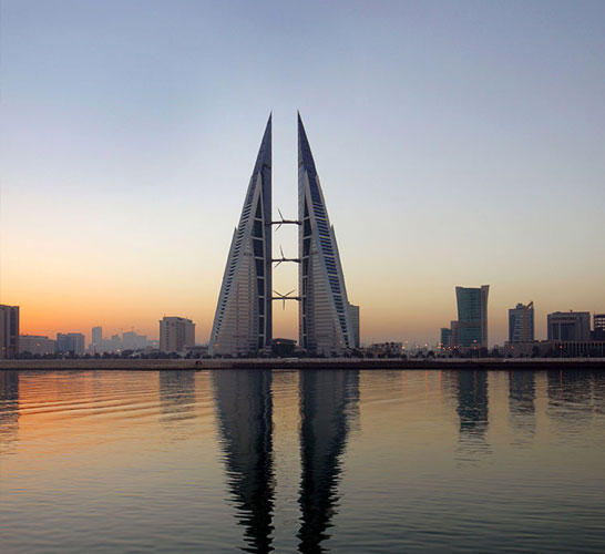 Image of a city in Bahrain with two symmetrical buildings side by side in the centre and a river in the foreground