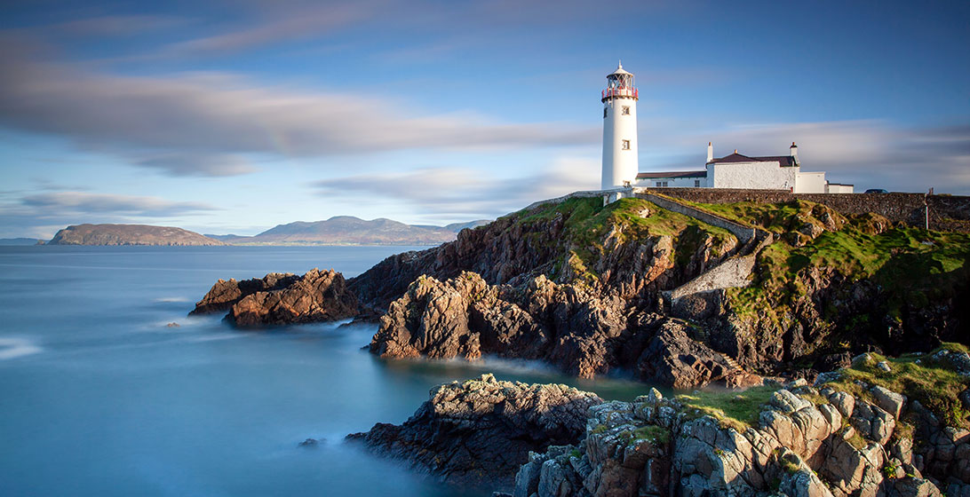 Photograph of a lighthouse on top of a rocky hill next to the sea