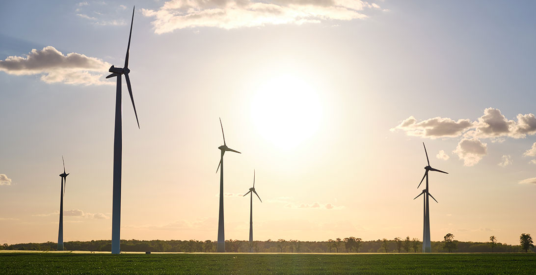 Photograph of a group of wind turbines with the sun shining above them