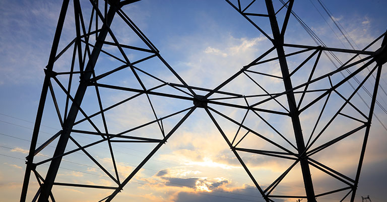 Photograph of a section of an electricity pylon silhouetted against a sunset