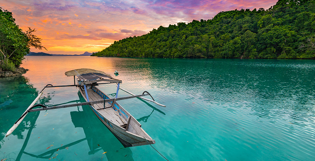 Photograph of a wooden boat on a river with forest and a sunset in the background