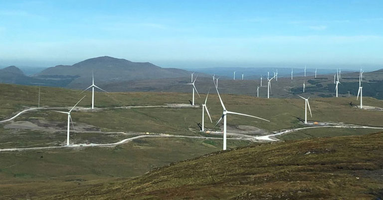 Photograph of a windfarm on top of mountains with blue sky in the background