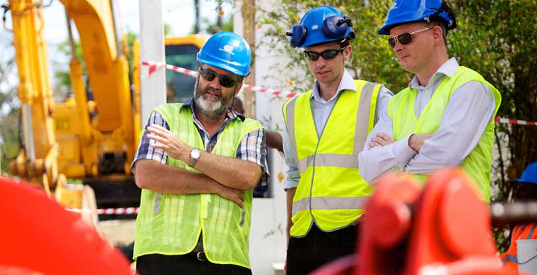 Photograph of three men in hard hats and high vis vests having a conversation