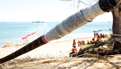 Photograph of a pipe leading onto a beach with workers at the end