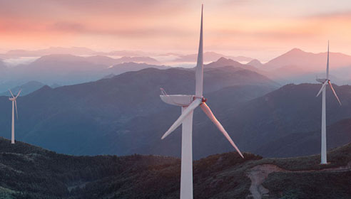 Photograph of a windfarm at the top of some mountains with the sun setting behind