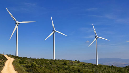 Image of four wind turbines on a hill with a dirt path in the foreground