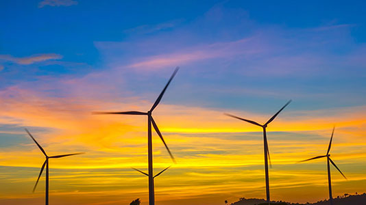 Photograph of wind turbines silhouetted against a sunset background