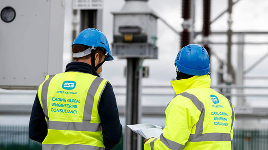 Image of the backs of two men on a site wearing hard hats and high vis jackets with the ESB International logo on it