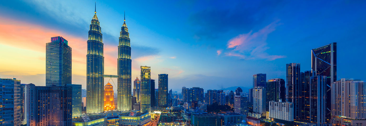 Photograph of the skyline in Kuala Lumpur. The sun is setting in the background
