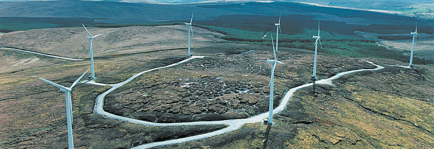 Aerial photograph of some wind turbines at the top of a mountain with a road running between them
