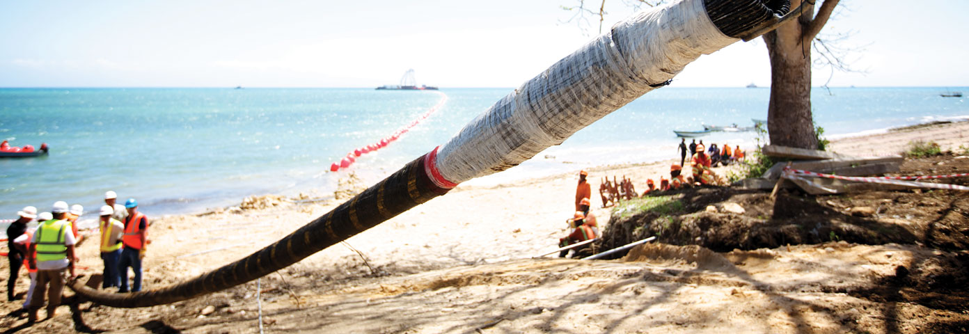 Photograph of a pipe leading onto a beach with workers at the end