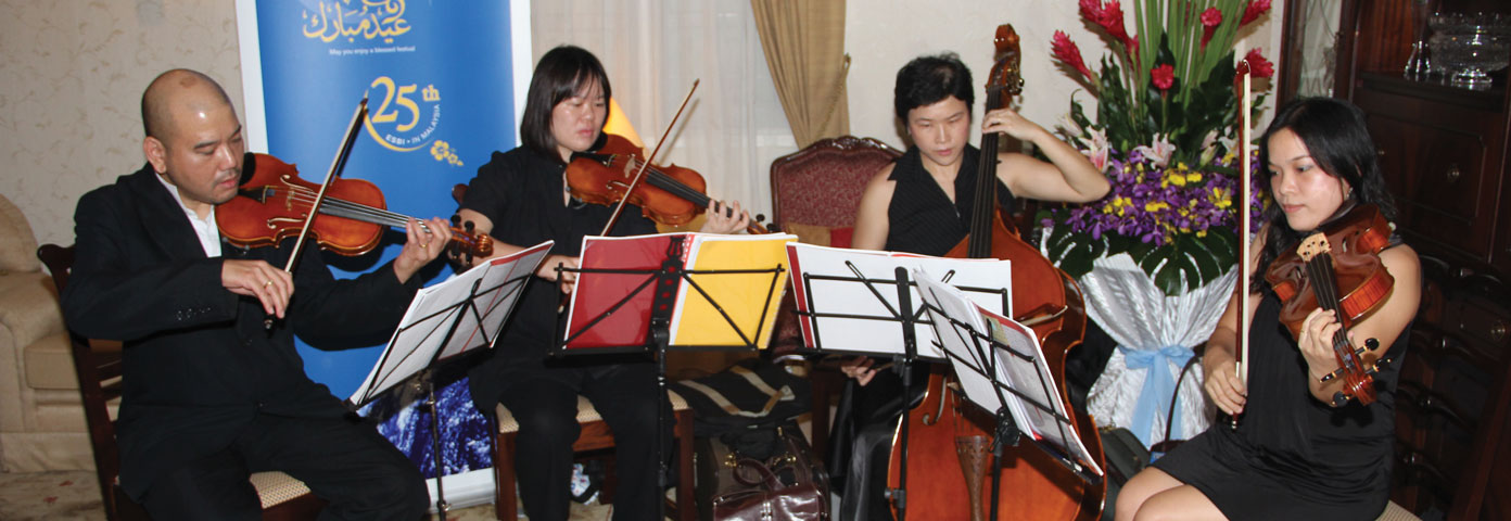 Photograph of one man and three women seated and playing string instruments