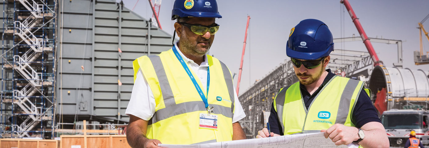 Image of two men in high vis vests and hard hats looking at some drawings on a building site