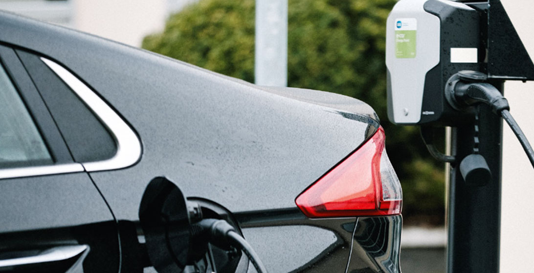 Photograph showing a black car with an electric charging cable plugged into it