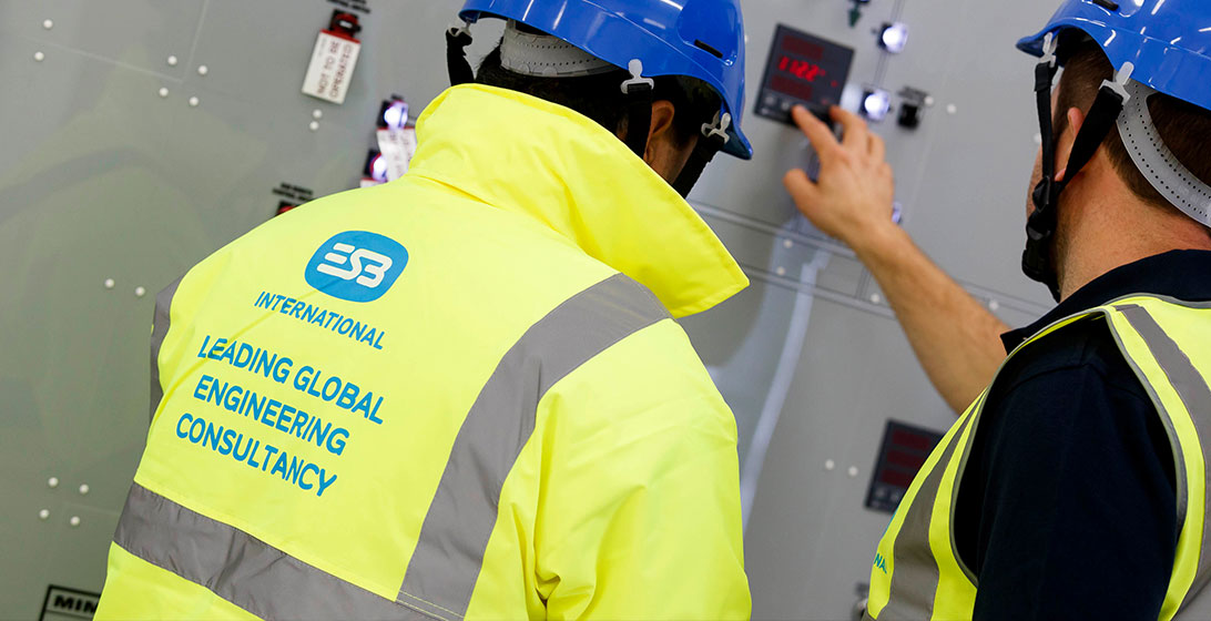 Photograph of two men in hard hats and high vis jackets. Their backs are to the camera and the man on the right is toughing a button on the wall panels