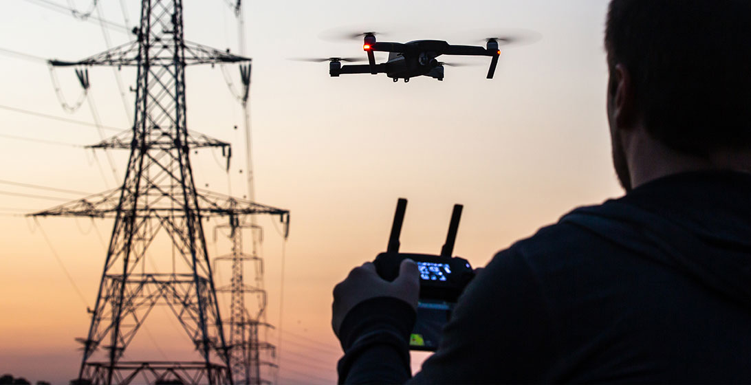 Photograph of a man flying a drone near some power lines